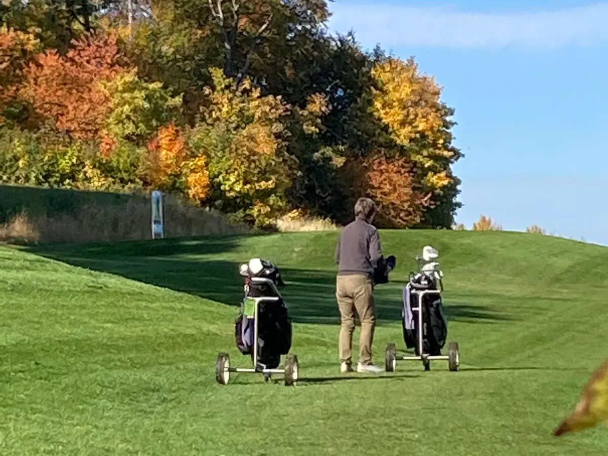 Zwei Golfer mit Trolleys auf dem Fairway im Herbst